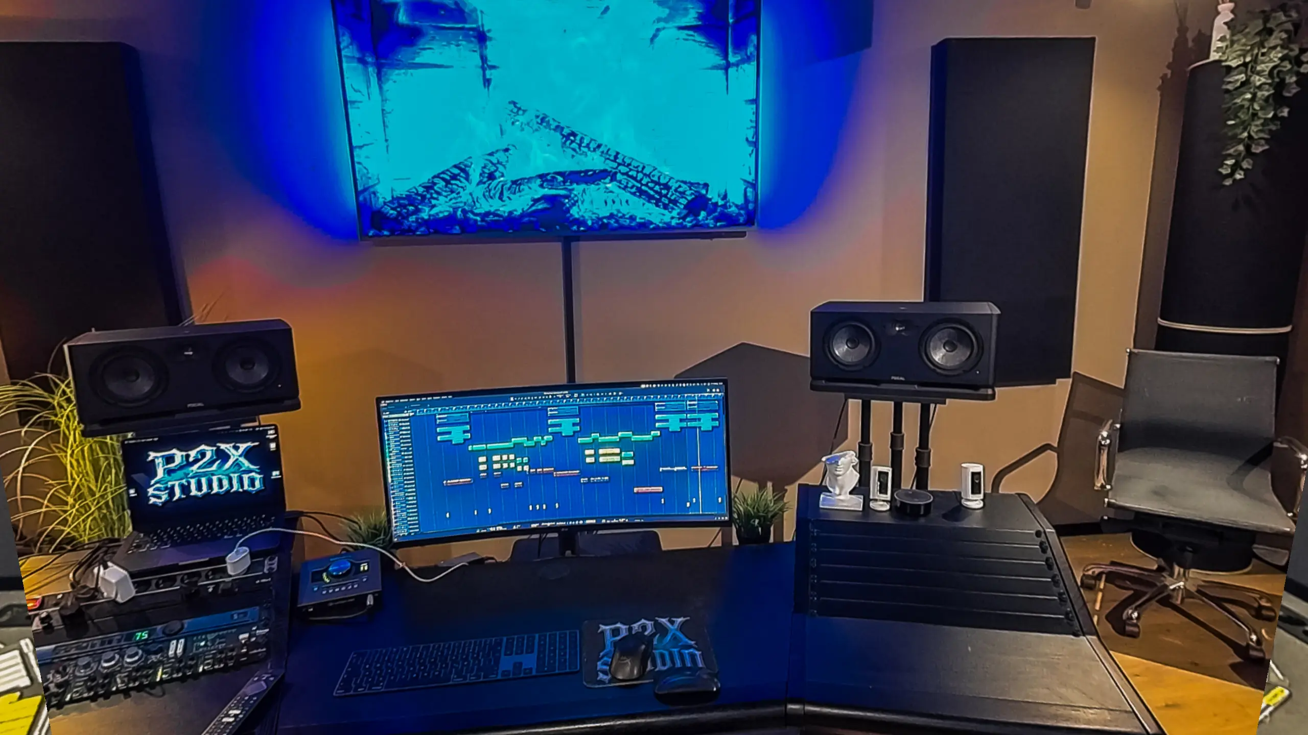 Der Regieplatz im P2X Studio: Nahfeldmonitore, laufende DAW auf dem Breitbildschirm, Rack mit Vorstufen und die blau hinterleuchtete Wand dahinter.